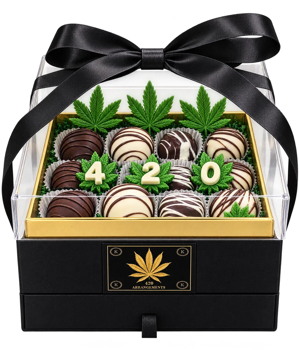The two-tier box under its clear lid, tied with a black satin ribbon, with white chocolate 4 2 0 pieces and green candy leaves inside.